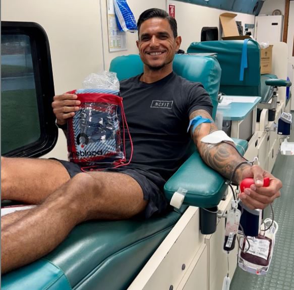 OneBlood donor with tattoos donating blood on a Big Red Bus showing off his OneBlood swag bag