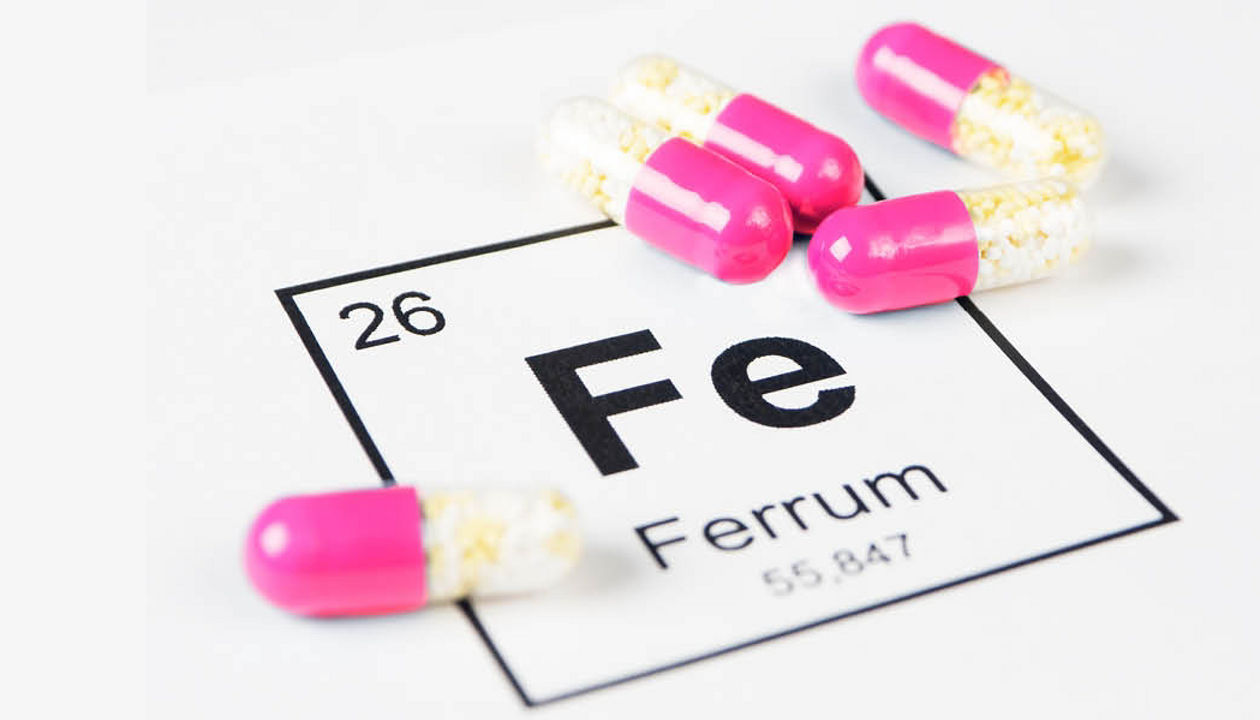 Pink iron supplement pills laying on top of an image of the periodic element for iron