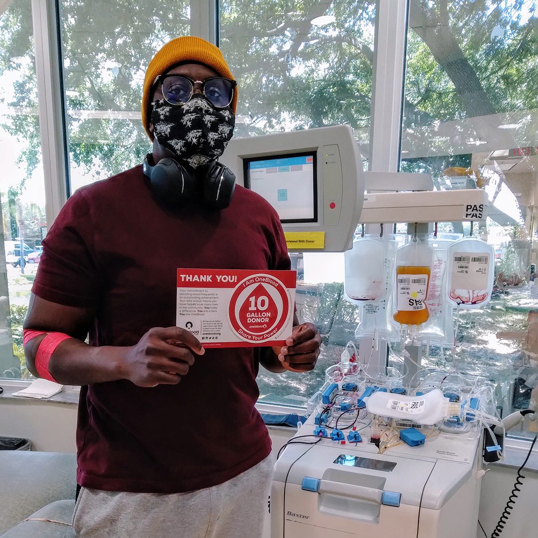 Jean holding 10 gallon milestone window cling in front of a platelet apheresis machine