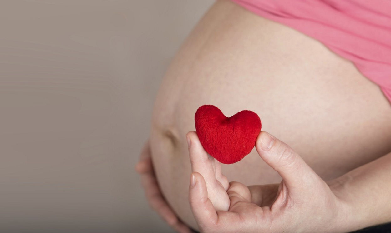 Pregnant woman holding a cloth heart next to her baby bump