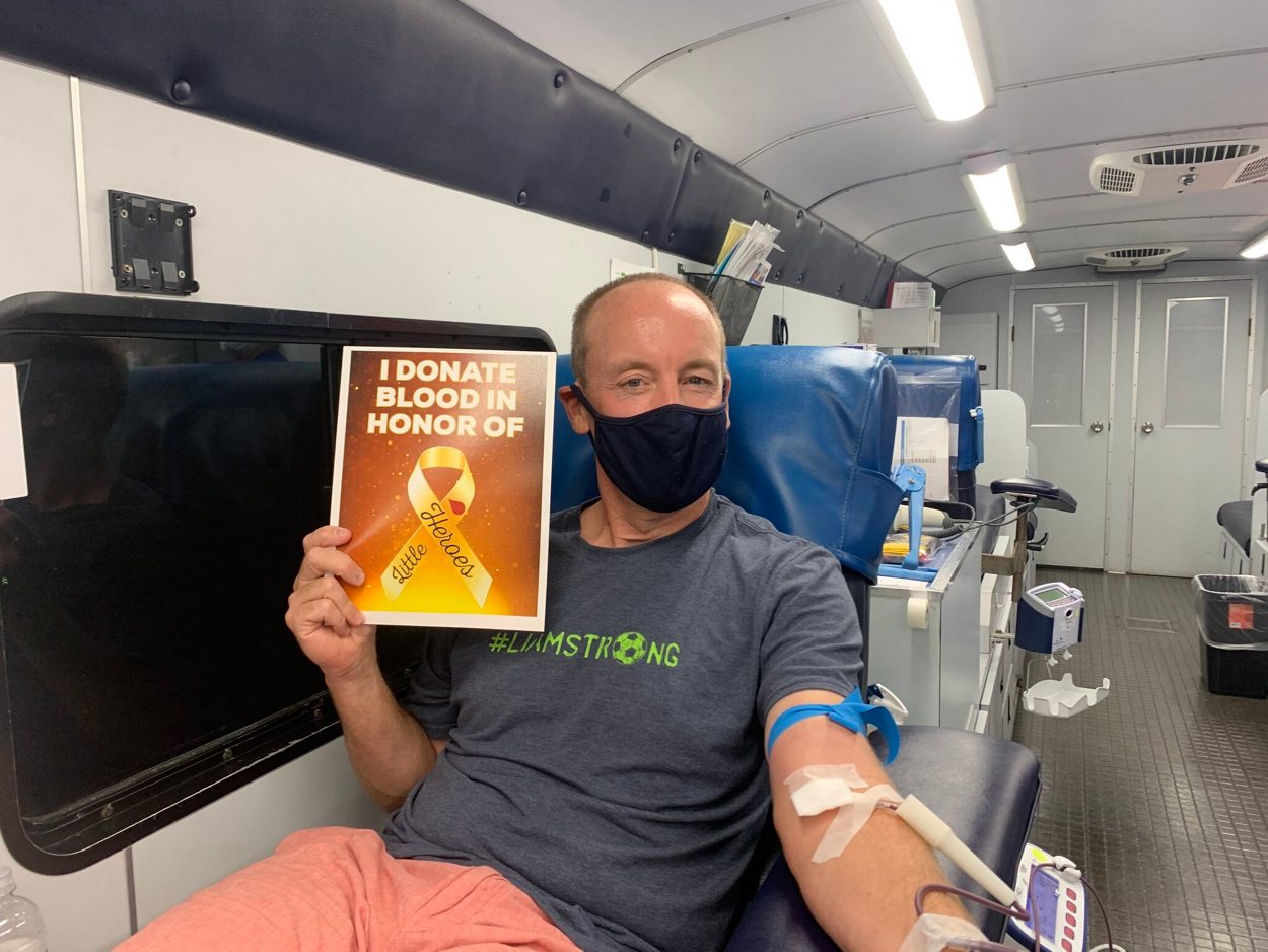 Shawn Flynn father of cancer survivor donating blood on big red bus blood drive