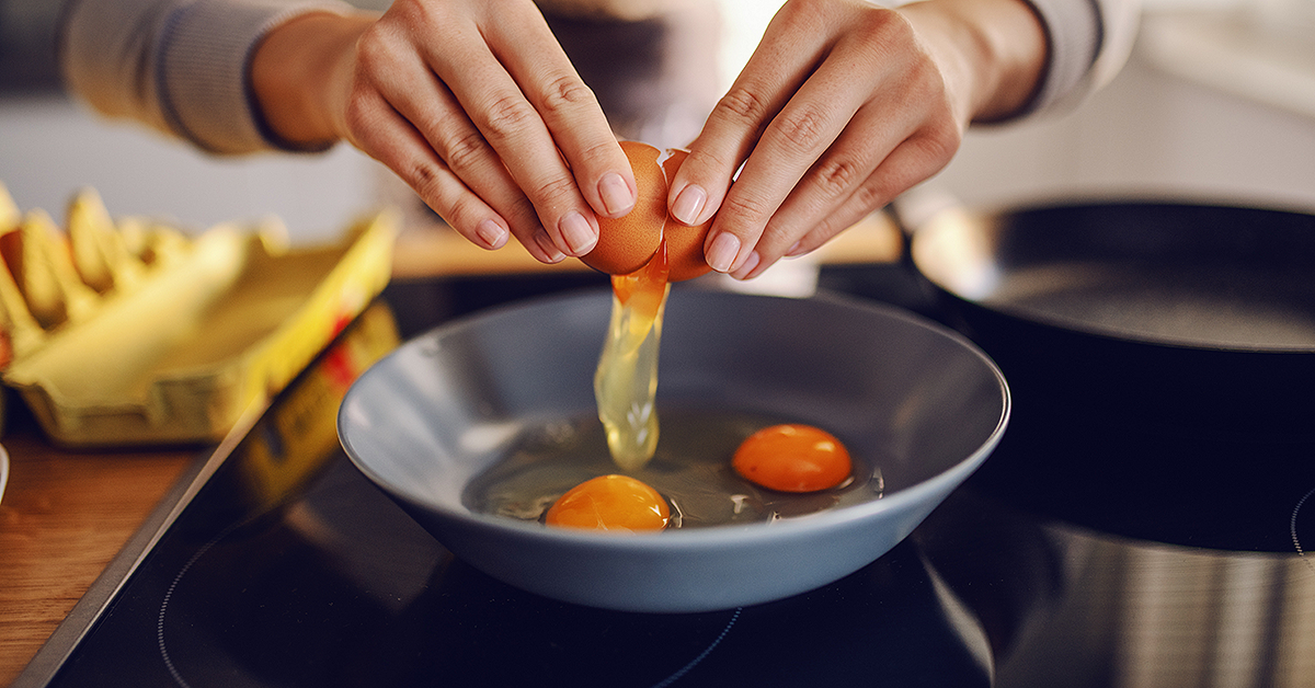 Close up of a woman cracking an egg into a frying pan