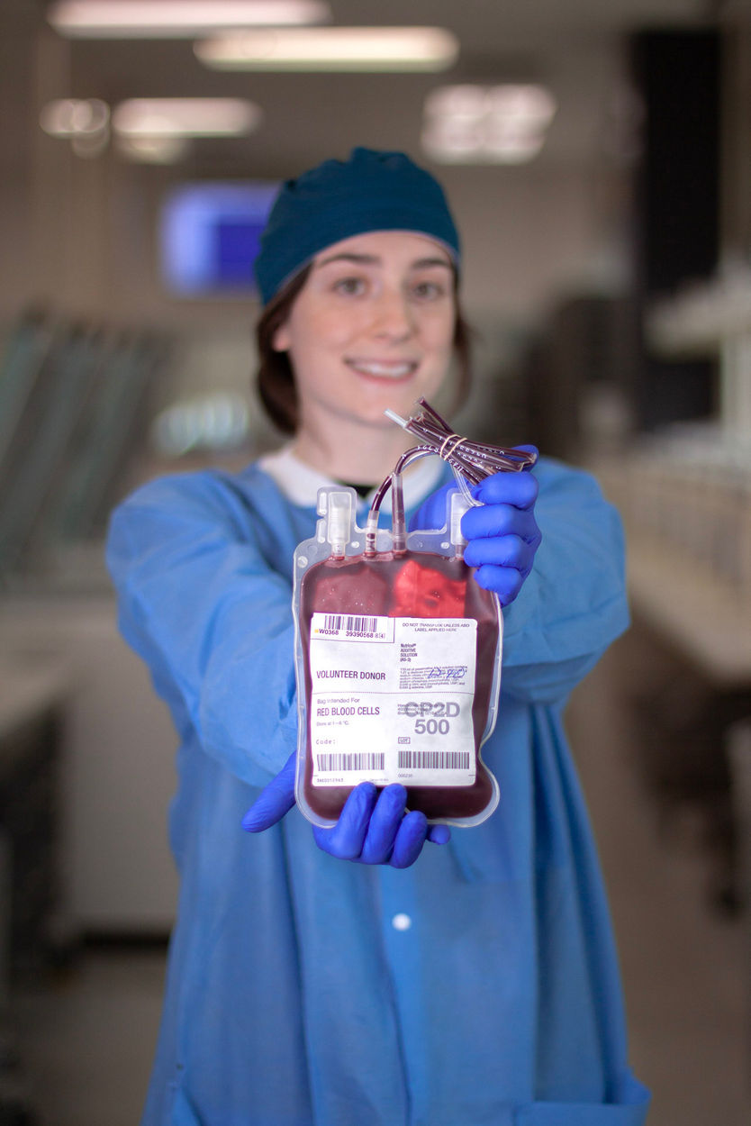 woman in scrubs and gloves holding blood bag