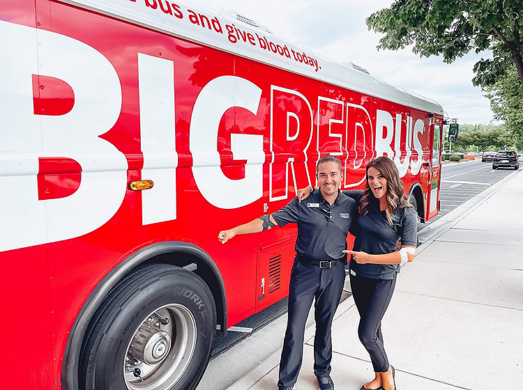 man and woman in front of the big red bus after donating