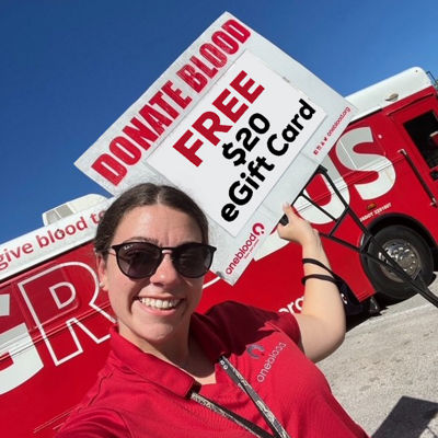 donor recruiter holding sign in front of Big Red Bus