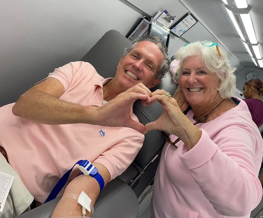 husband and wife donating blood on the big red bus, joined hands to form a heart