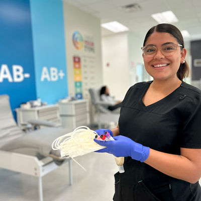 Phlebotomist standing in a donor room, holding an empty blood bag and some tube for blood samples