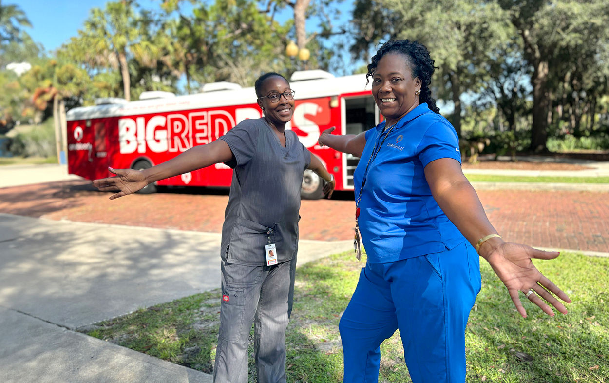 Phlebotomists welcoming donors with open arms in front of the Big Red Bus