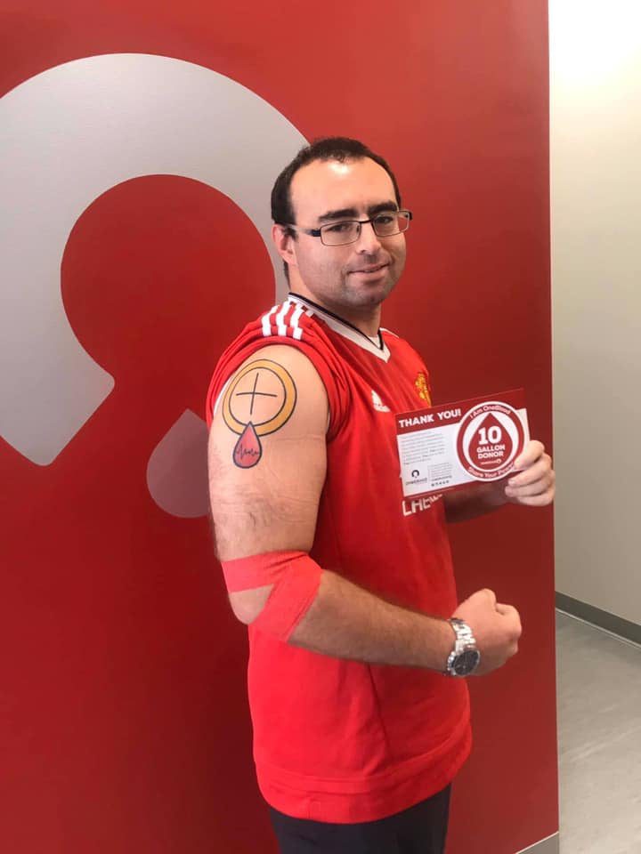 blood donor with tattoo on arm holding donor milestone sticker