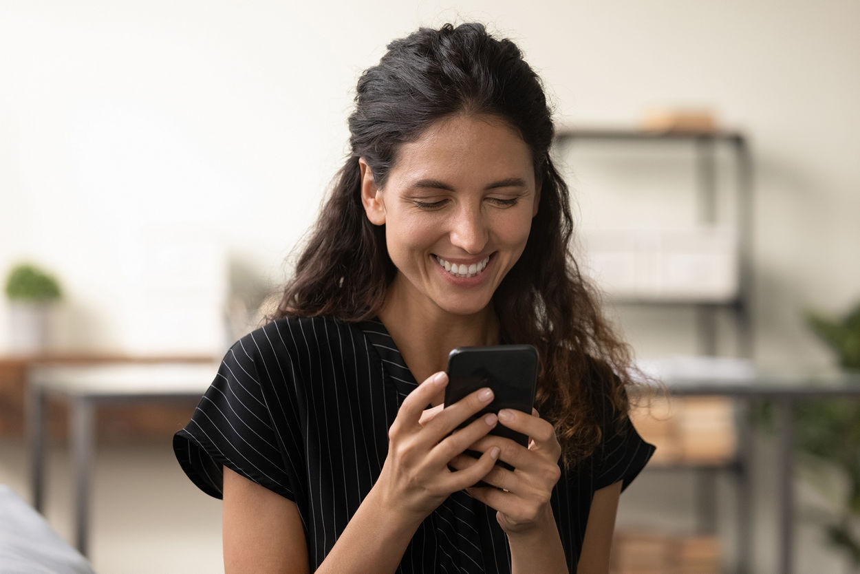 Good message. Smiling young hispanic lady reading positive news in email on phone screen at home or in office. Happy millennial latin woman enjoy chatting in social media relax online playing web game