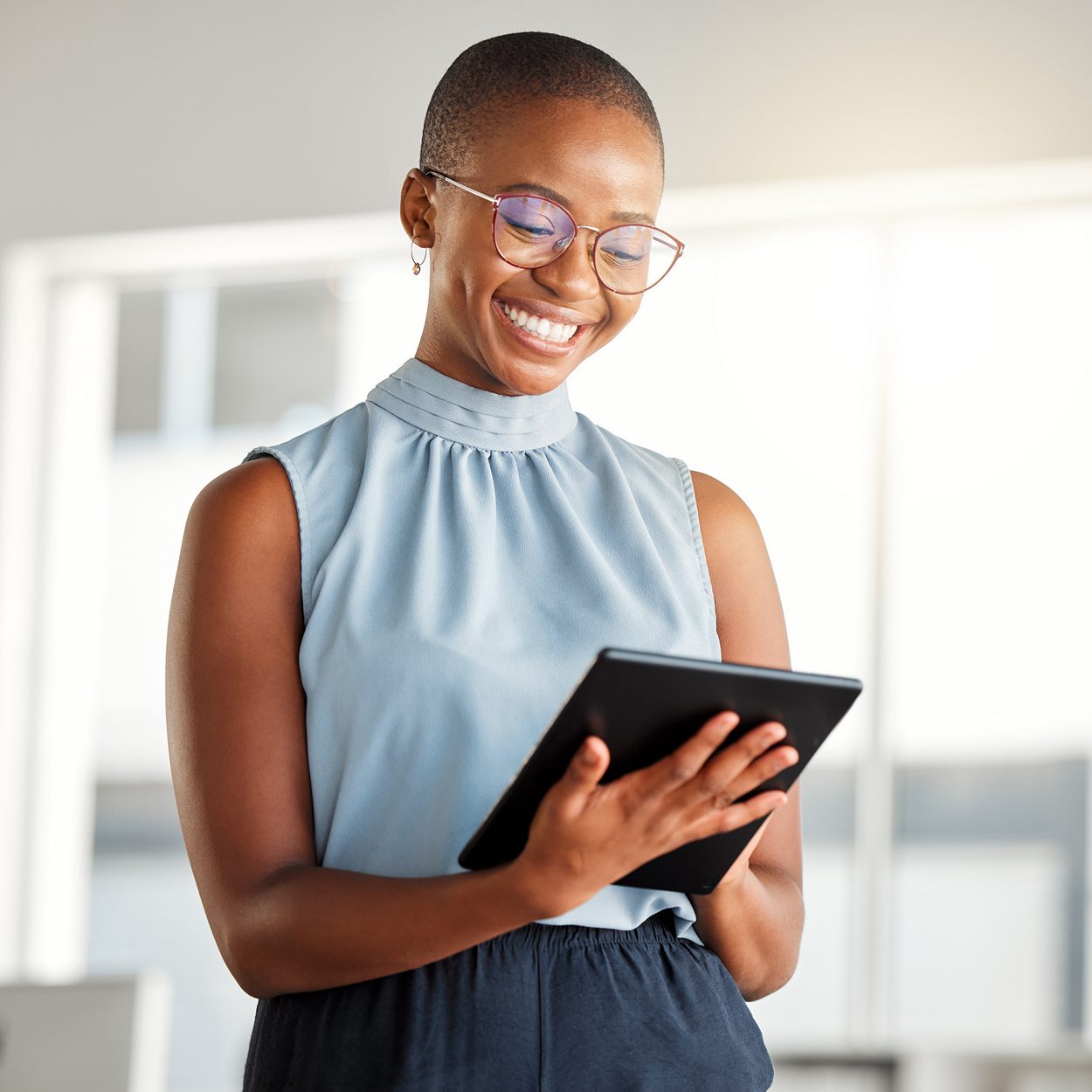 Young cheerful african american businesswoman working on a digital tablet alone at work. Happy black woman smiling while using social media on a digital tablet. Businessperson checking an email on a digital tablet